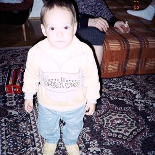 Baby stands near an elderly woman, toys on floor.