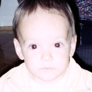 Baby stands near an elderly woman, toys on floor.