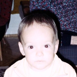 Baby stands near an elderly woman, toys on floor.