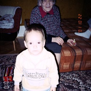 Baby stands near an elderly woman, toys on floor.