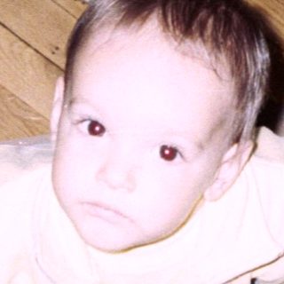 Infant standing on patterned rug, viewed from above.