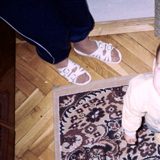 Infant standing on patterned rug, viewed from above.