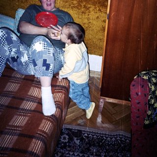 Man on couch interacts with a toddler holding a plate.