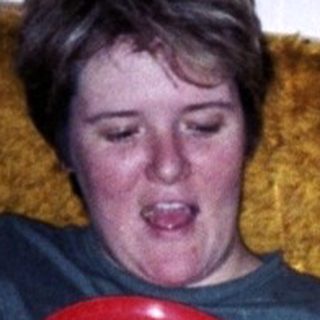 Man on couch interacts with a toddler holding a plate.