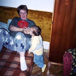 Man on couch interacts with a toddler holding a plate.