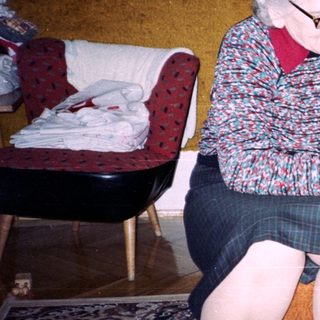 An elderly woman sits with a baby on a couch.