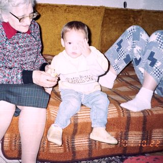 An elderly woman sits with a baby on a couch.