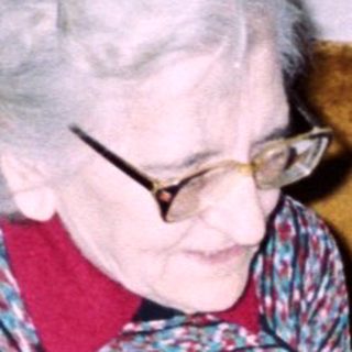 An elderly woman sits with a baby on a couch.