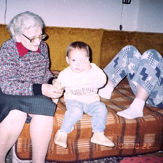 An elderly woman sits with a baby on a couch.