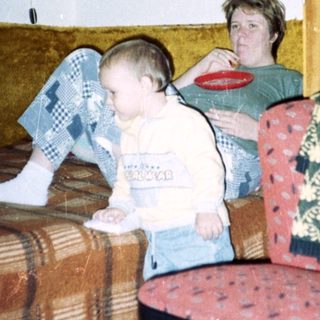 Young child sits near an adult in a patterned room.
