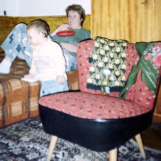 Young child sits near an adult in a patterned room.