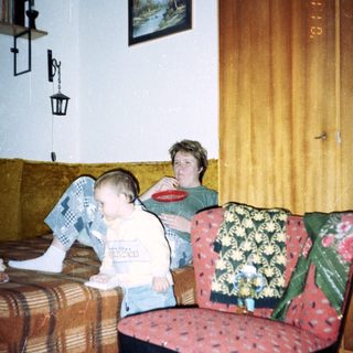 Young child sits near an adult in a patterned room.