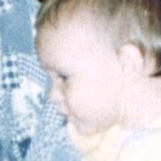 Young child sits near an adult in a patterned room.