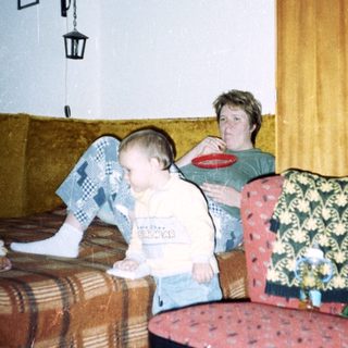 Young child sits near an adult in a patterned room.