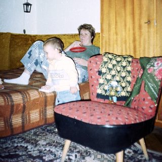 Young child sits near an adult in a patterned room.