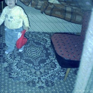 Child stands on rug, with person lying on couch.