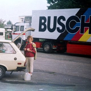 Boy stands next to car, truck with "BUSCH" logo.