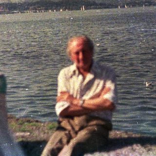 Man sits near water, overlooking a distant shoreline.