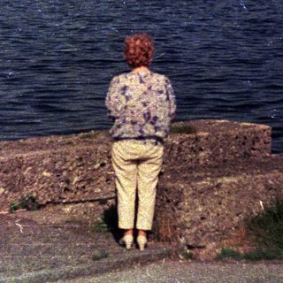 Person views sailboats on water from a stone wall.