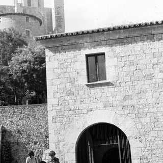 People near a stone building with a tower in background.