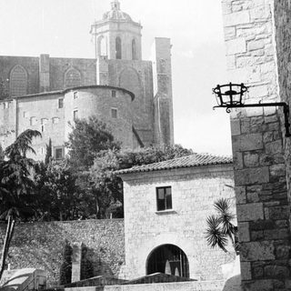 Stone buildings and a tower are seen from below.