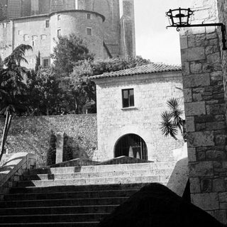 Stone buildings and a tower are seen from below.