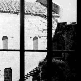 Here's a brief summary of the image: Stone building with arches, steps, and overgrown vegetation visible.