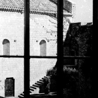 Here's a brief summary of the image: Stone building with arches, steps, and overgrown vegetation visible.