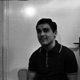 Here's a brief summary of the image: Man in a polo shirt smiles, seated near a door.