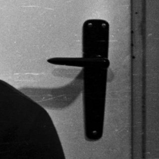 Here's a brief summary of the image: Man in a polo shirt smiles, seated near a door.