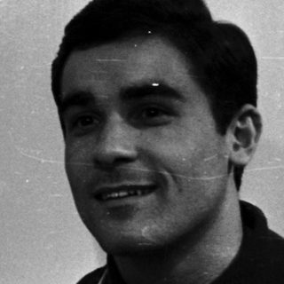 Here's a brief summary of the image: Man in a polo shirt smiles, seated near a door.