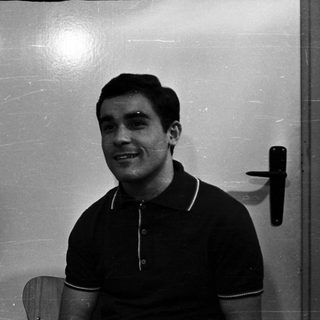 Here's a brief summary of the image: Man in a polo shirt smiles, seated near a door.