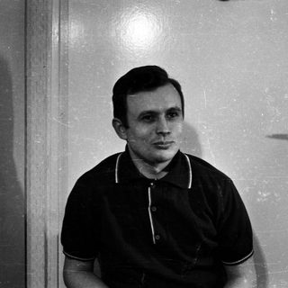 Man in polo shirt stands near a door.