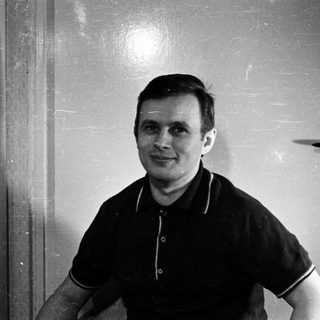 Man in a polo shirt stands near a door.