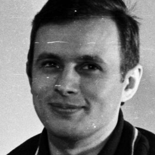 Man in a polo shirt stands near a door.