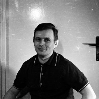 Man in a polo shirt stands near a door.