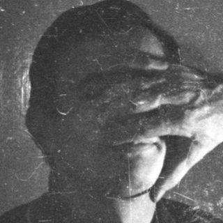 Person blocking their face with their hand, near a door.