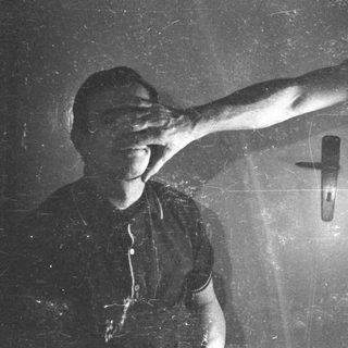Person blocking their face with their hand, near a door.