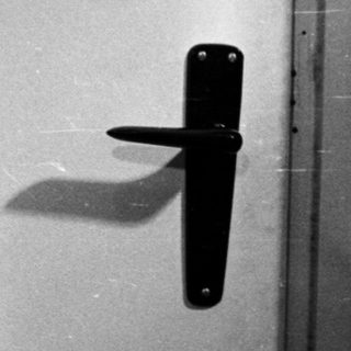 Black and white portrait of a man standing near a door.