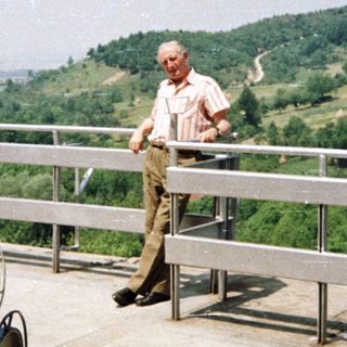 Man stands on a rooftop overlooking a hillside landscape.