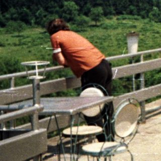 Two people on a terrace overlooking a forested, hilly landscape.