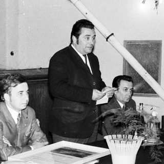 Panel discussion with audience, speaker, and potted plants.