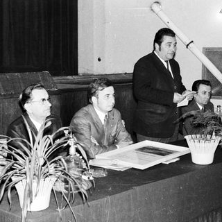 Panel discussion with audience, speaker, and potted plants.