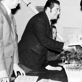 Two men handing a document to a third, formal setting.