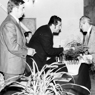 Here's a brief summary of the image: Men in suits appear to exchange gifts at an event.