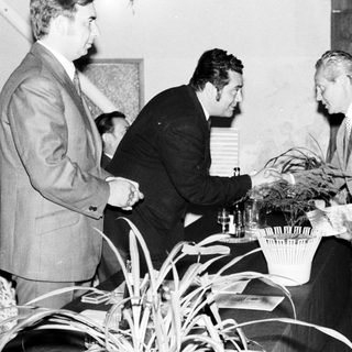 Here's a brief summary of the image: Men in suits appear to exchange gifts at an event.