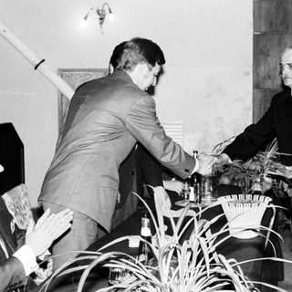 Two men shake hands in a formal, black and white setting.