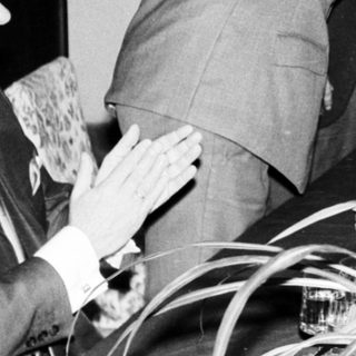 Two men shake hands in a formal, black and white setting.