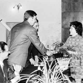 Man serves drinks to a woman in a patterned dress.