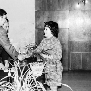 Man serves drinks to a woman in a patterned dress.
